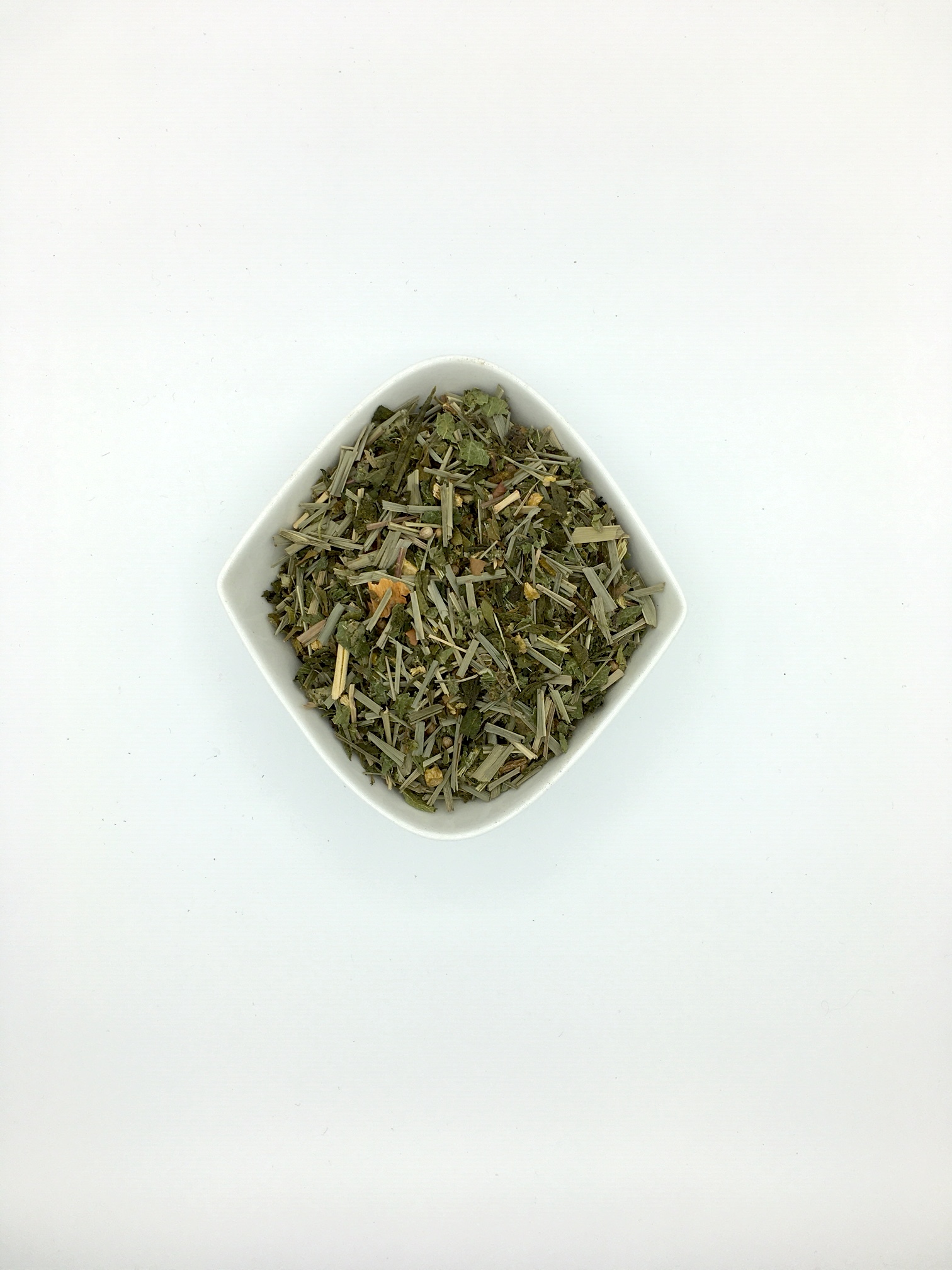 Die weiße rautenförmige Porzellanschale enthält mittelgrob geschnittene grau-grüne Kräuter und gelbliche Gewürzstückchen.