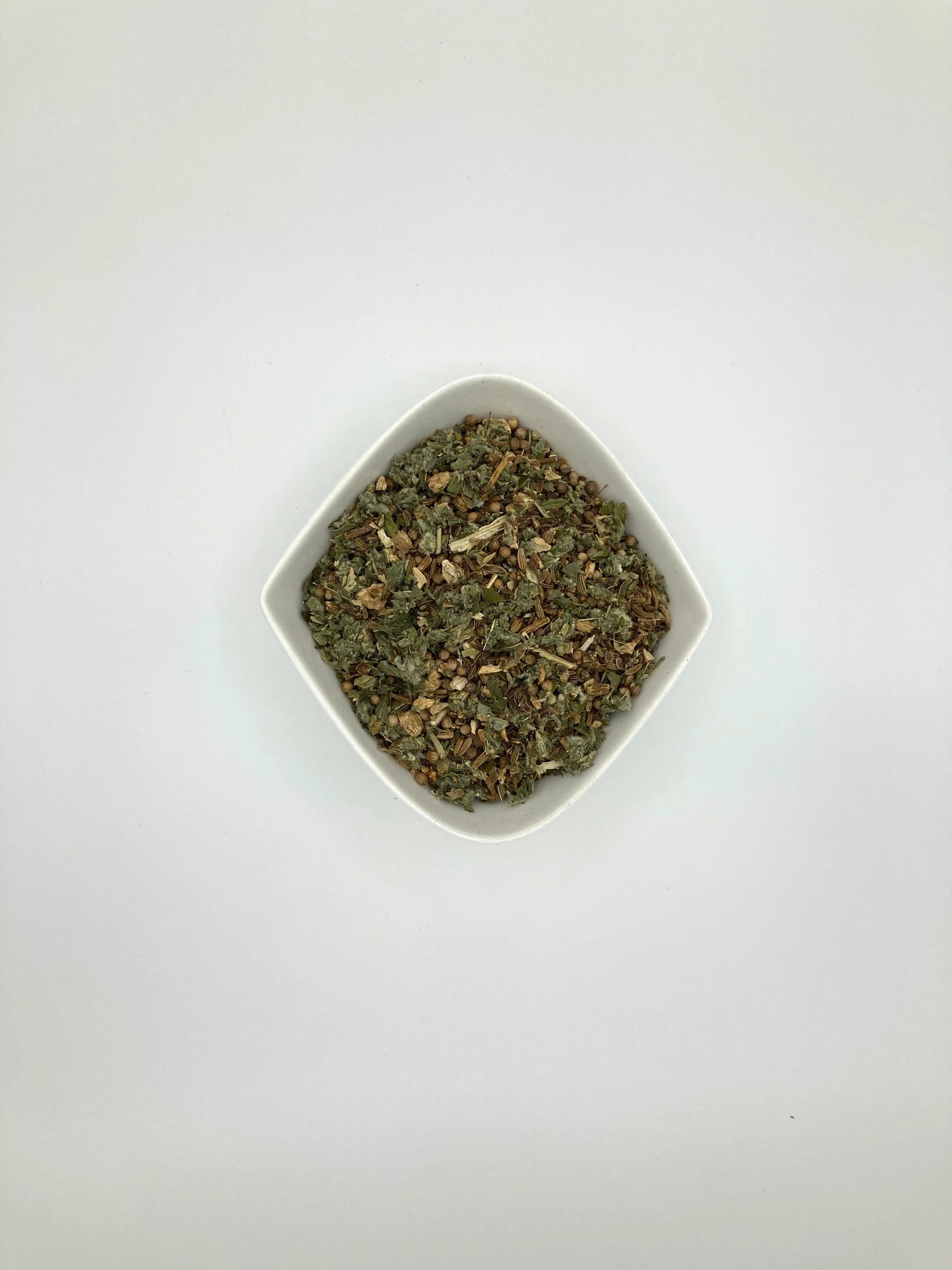 Die weiße rautenförmige Porzellanschale enthält grün-graue mittelgrob geschnittene Blätter und gelb-braune Gewürzstückchen
