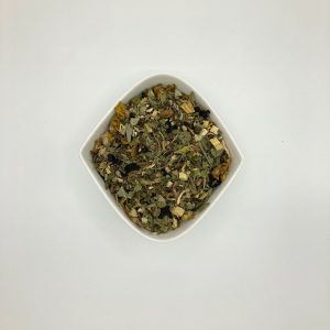 Die weiße rautenförmige Porzellanschale enthält dunkelgrüne Blattstückchen und gelbe Blüten und helle Wurzelstücke.