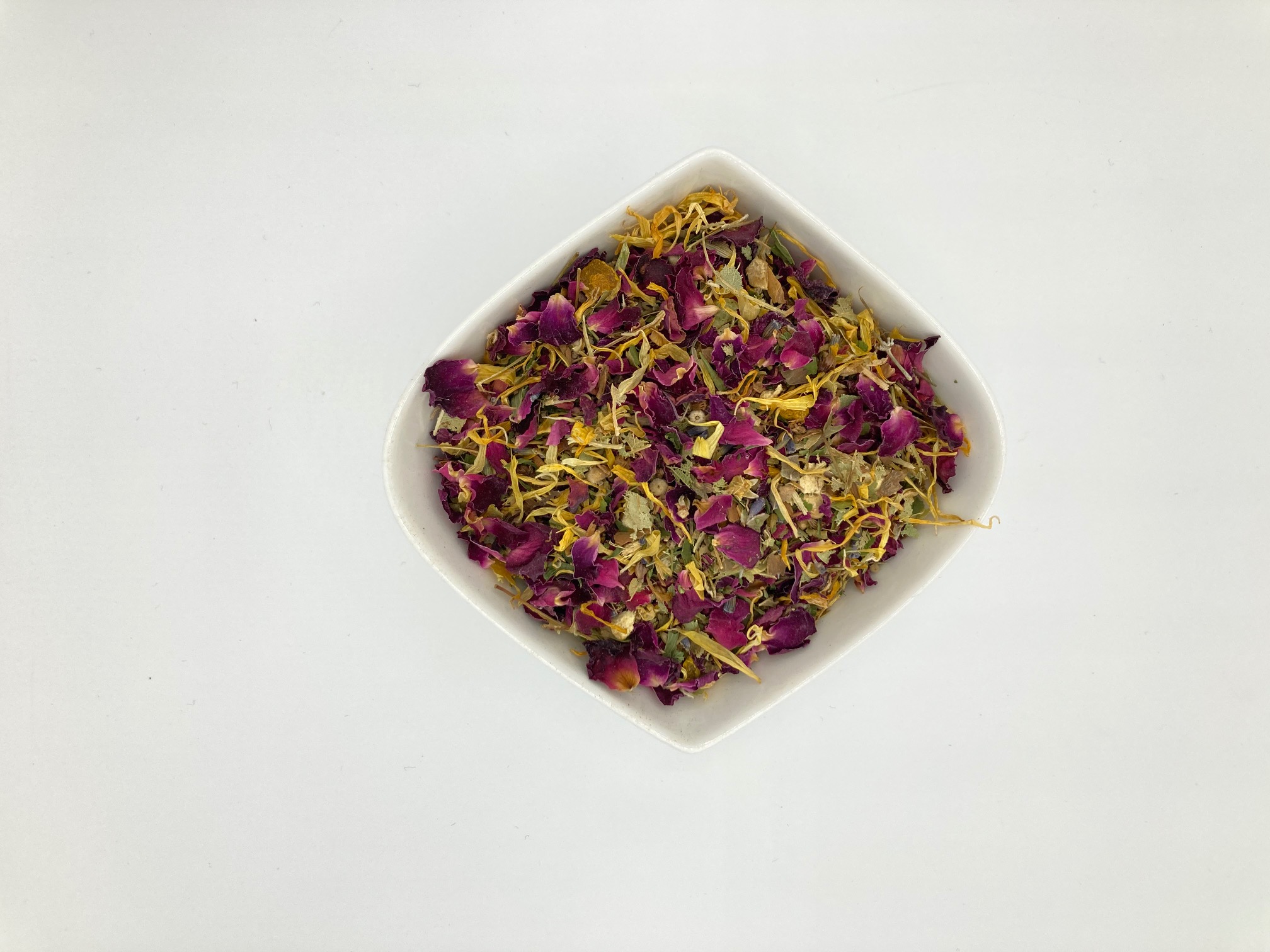 Die weiße rautenförmige Porzellanschale enthält vorwiegend gelbe und magentafarbene Blütenblätter.