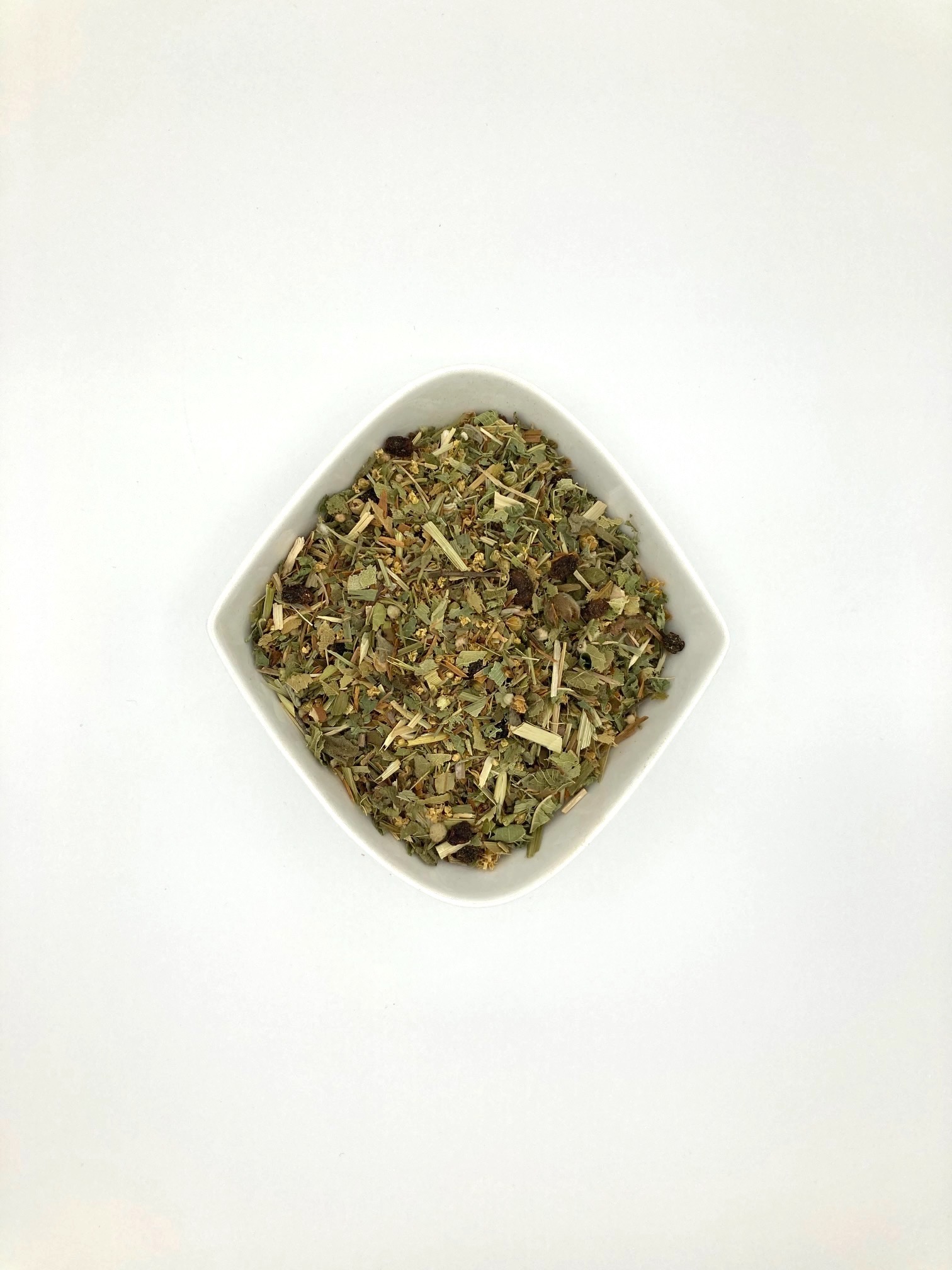 rautenförmige weiße Porzellanschale mit fein geschnittenen Kräutern und getrockneten Beeren